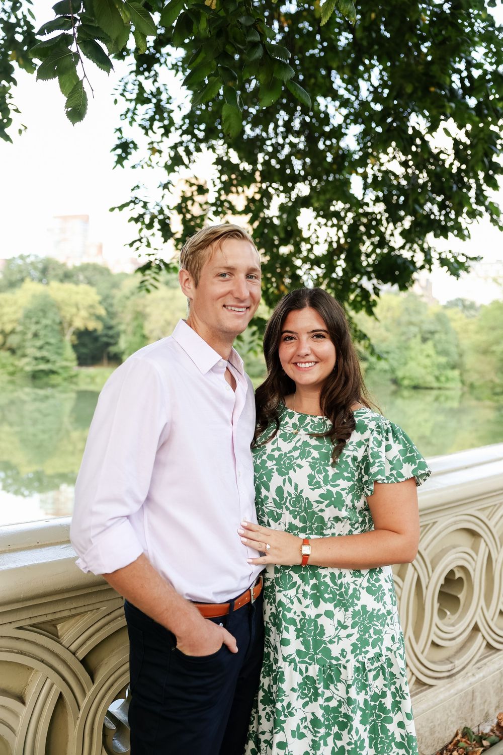 Couple laughing together while posing on an ornate stone bridge with lush greenery in the background.