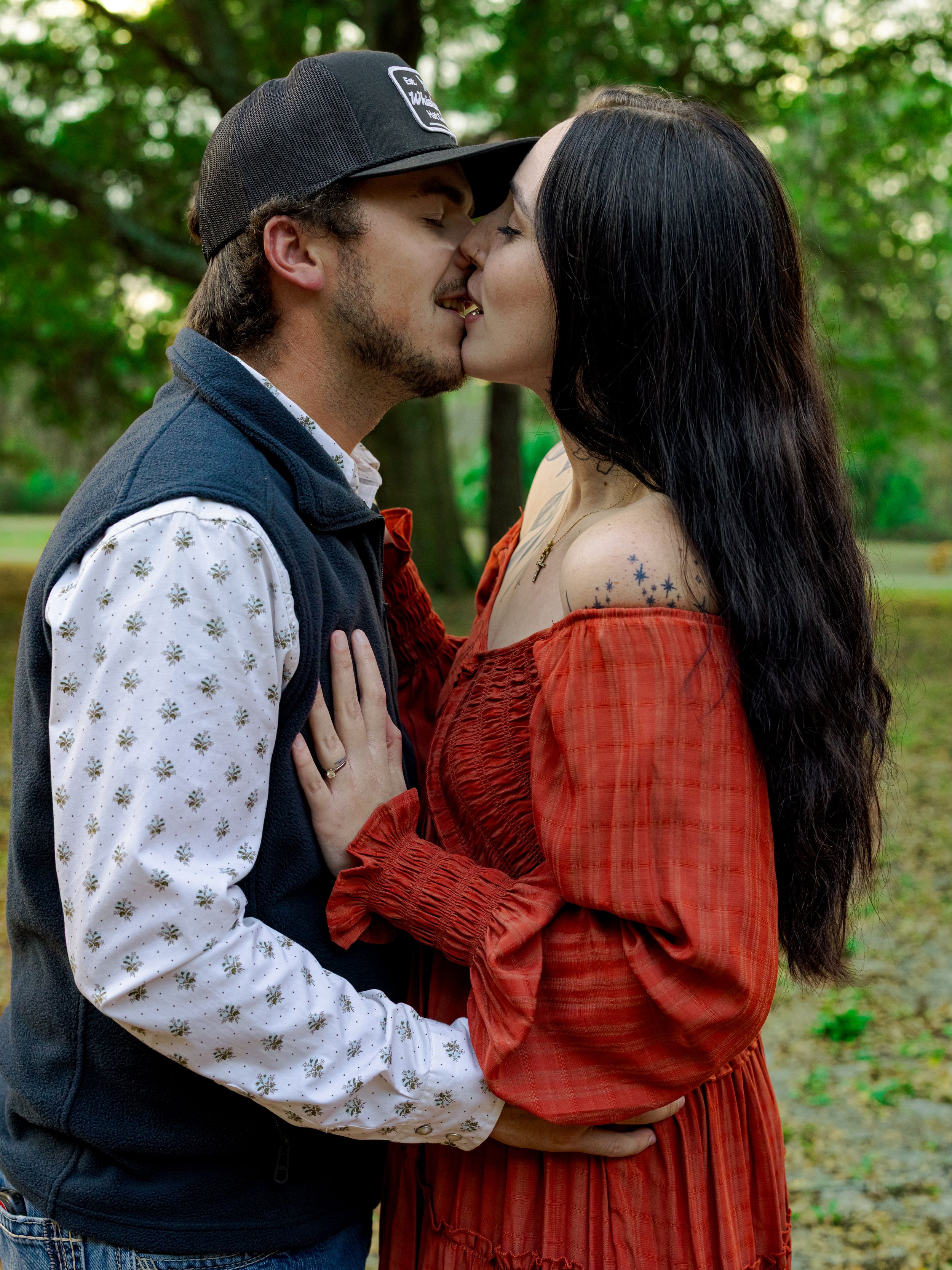 Couple sharing a romantic kiss outdoors in a lush green park setting.