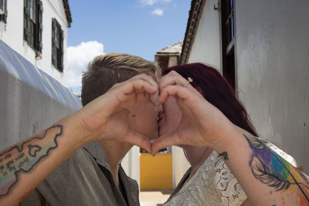 Tattooed couple kissing while making a heart shape with their hands outdoors.