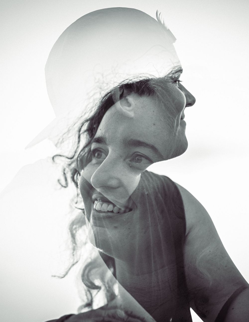 A black and white double exposure portrait of a smiling young woman merged with a silhouette profile image.