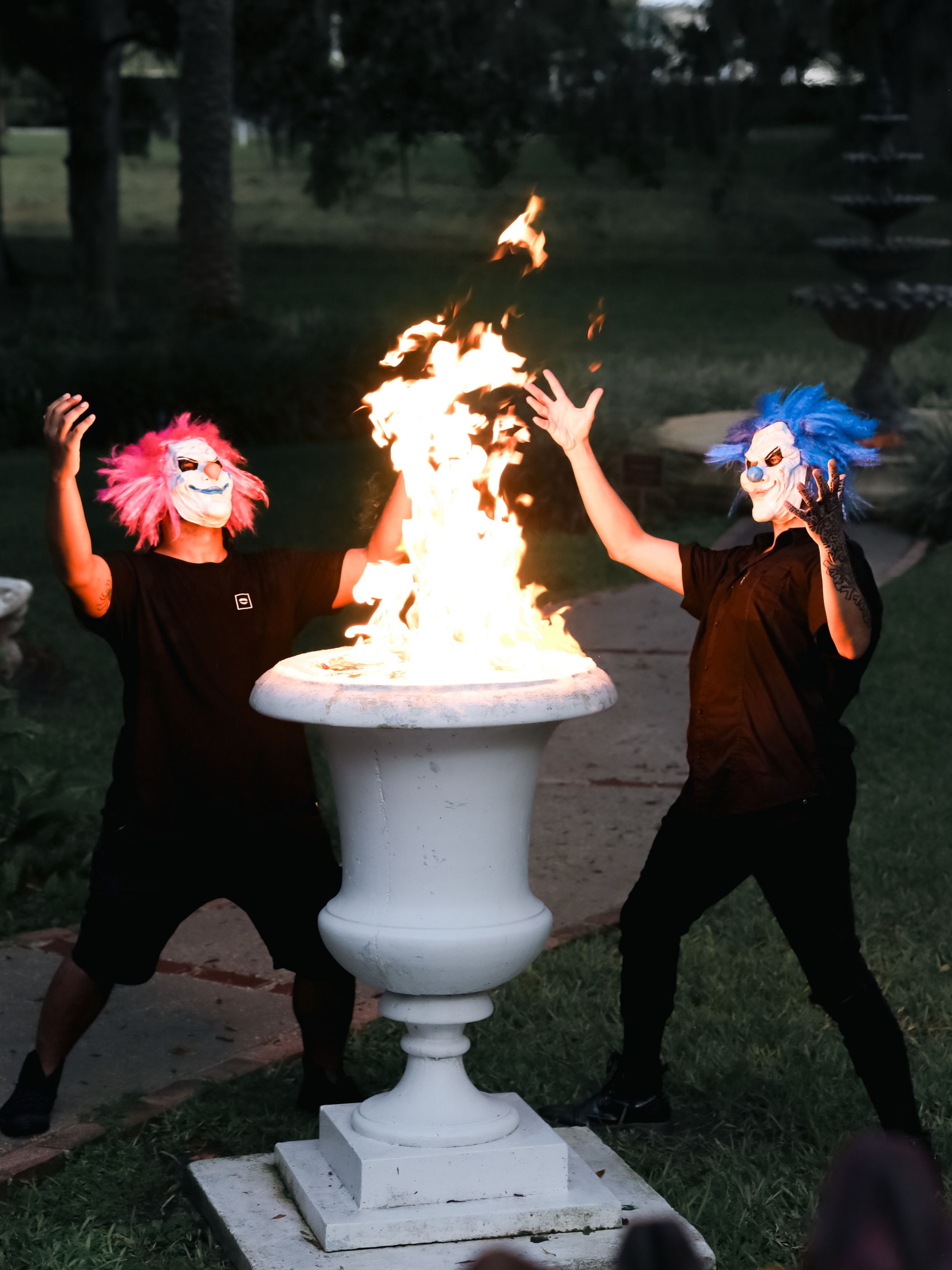 Two masked performers in black near a flaming urn at dusk.