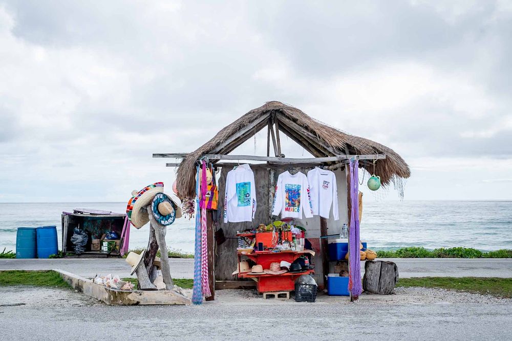 Beachside souvenir stand with thatched palm roof selling colorful clothing and beach items near the ocean in Cozumel, Mexico.