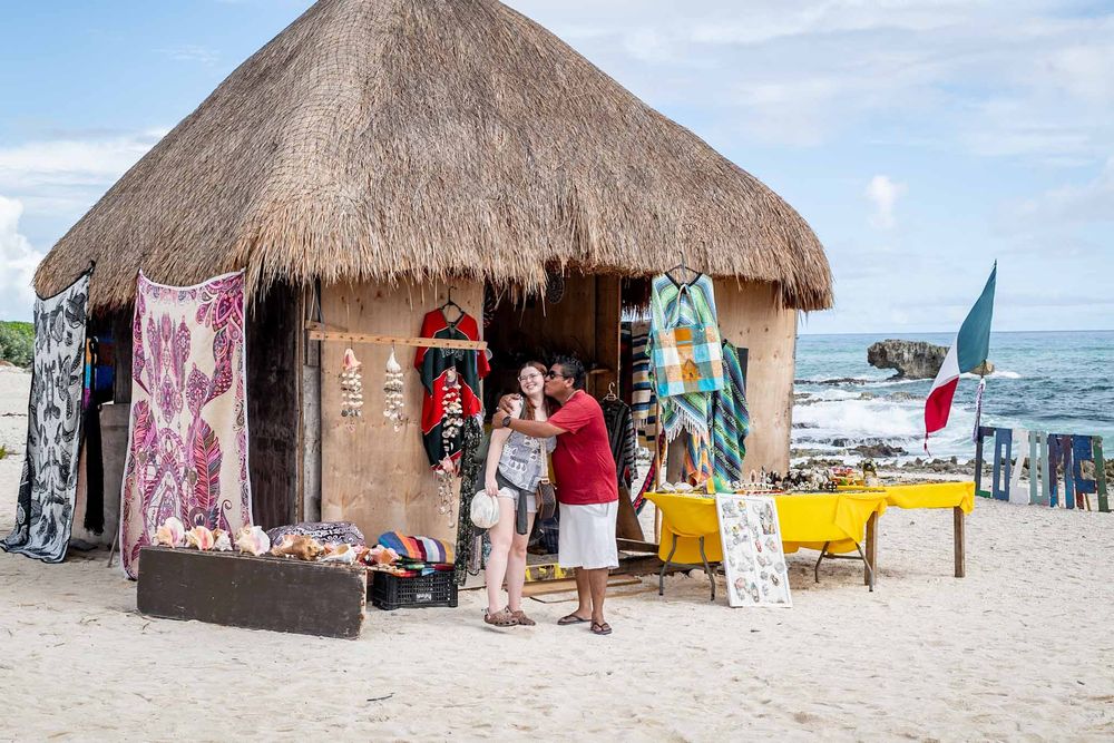 Beach vendors display colorful souvenirs and merchandise under thatched-roof huts along a tropical shoreline in Cozumel, Mexico.