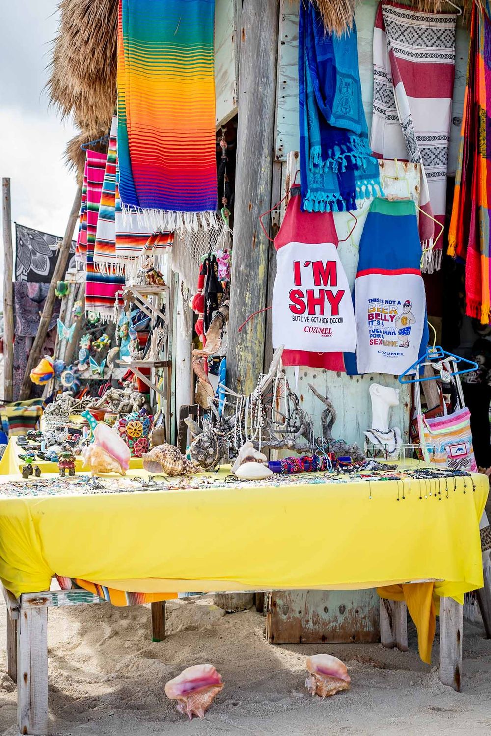 Colorful Mexican blankets and souvenirs displayed at outdoor market stalls with yellow countertops.