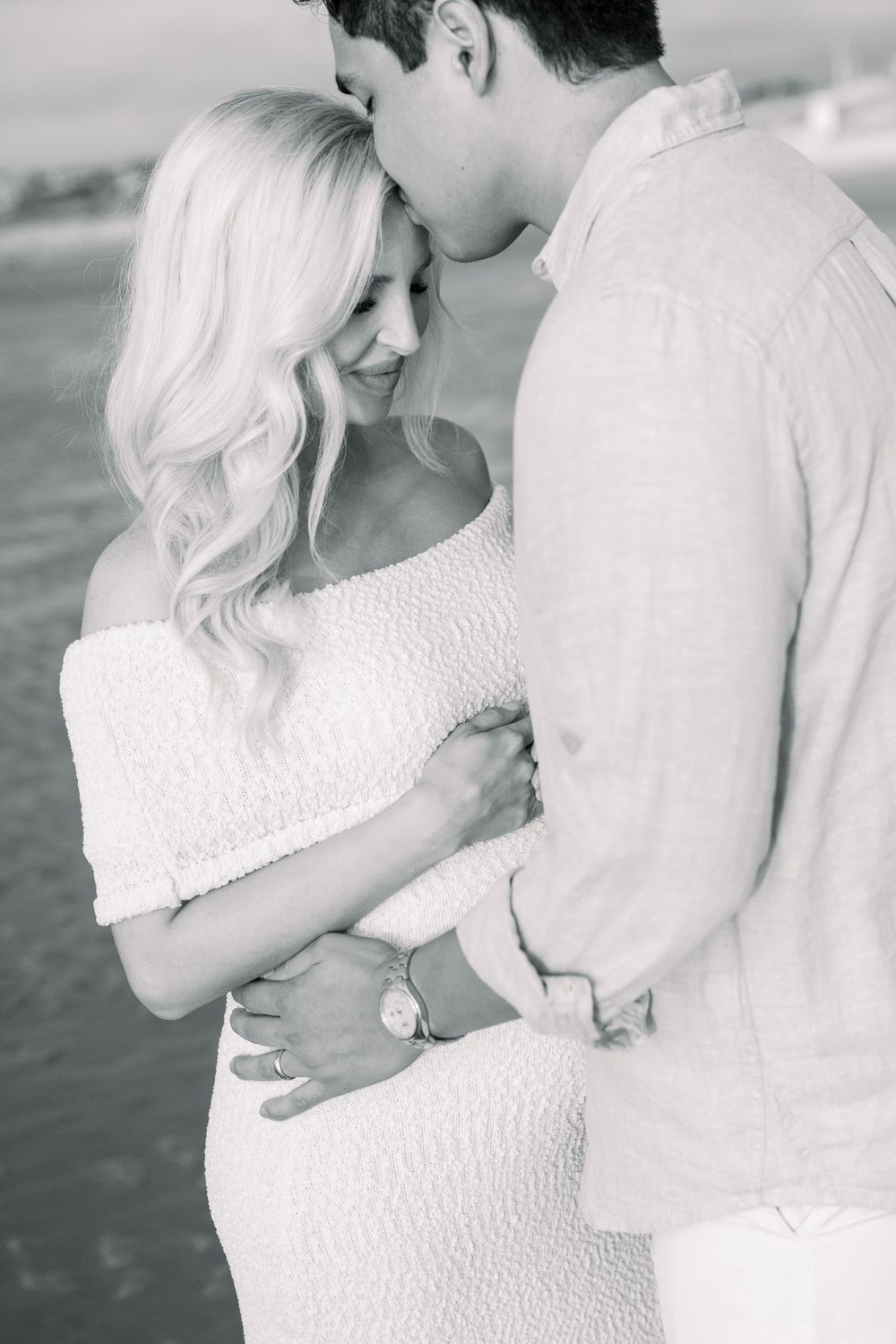 A romantic black and white portrait shows a couple embracing intimately, with her wearing a textured white dress.