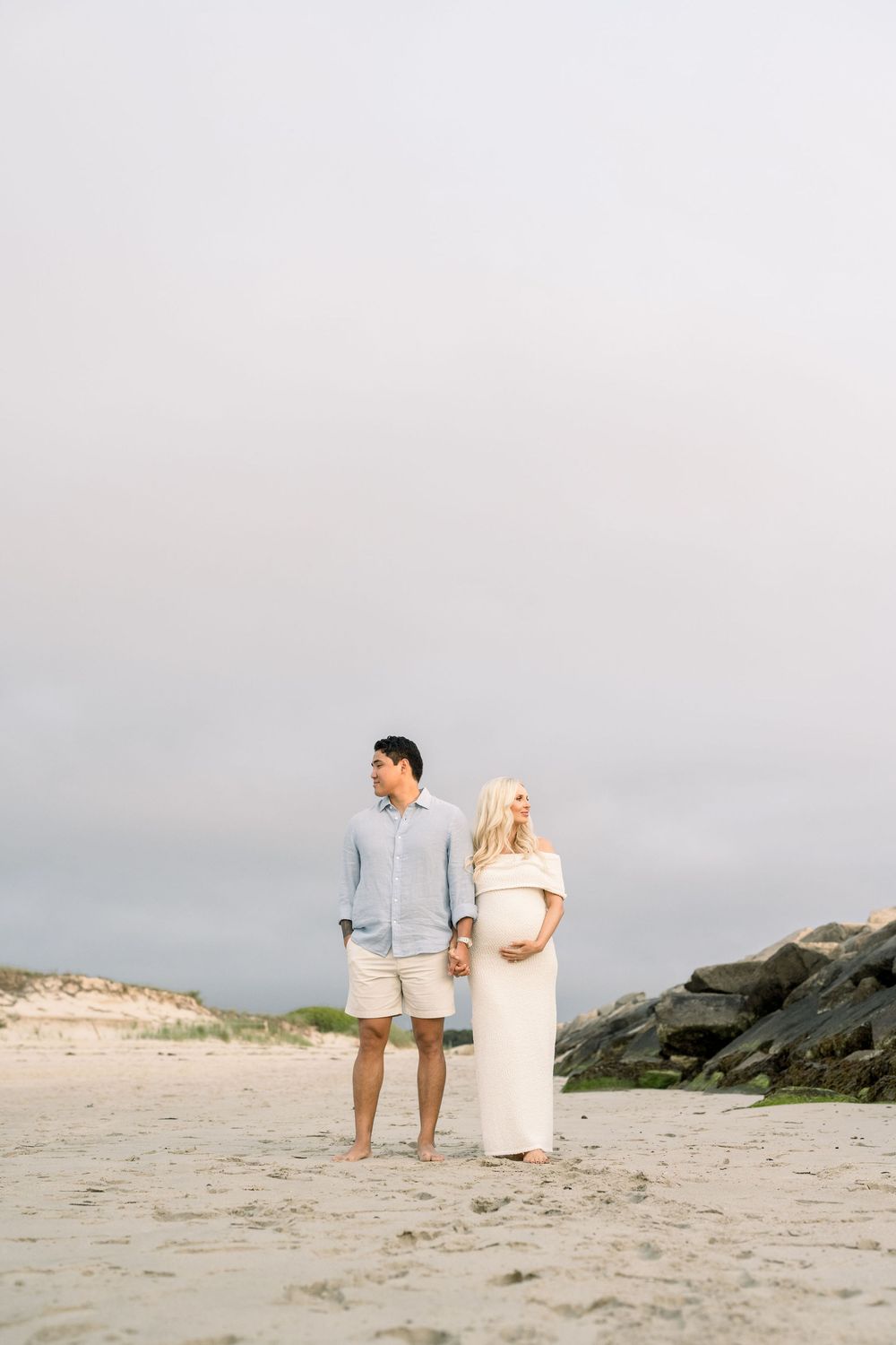 A couple walks hand in hand along a scenic beach during sunset, creating romantic silhouettes against the cloudy sky.