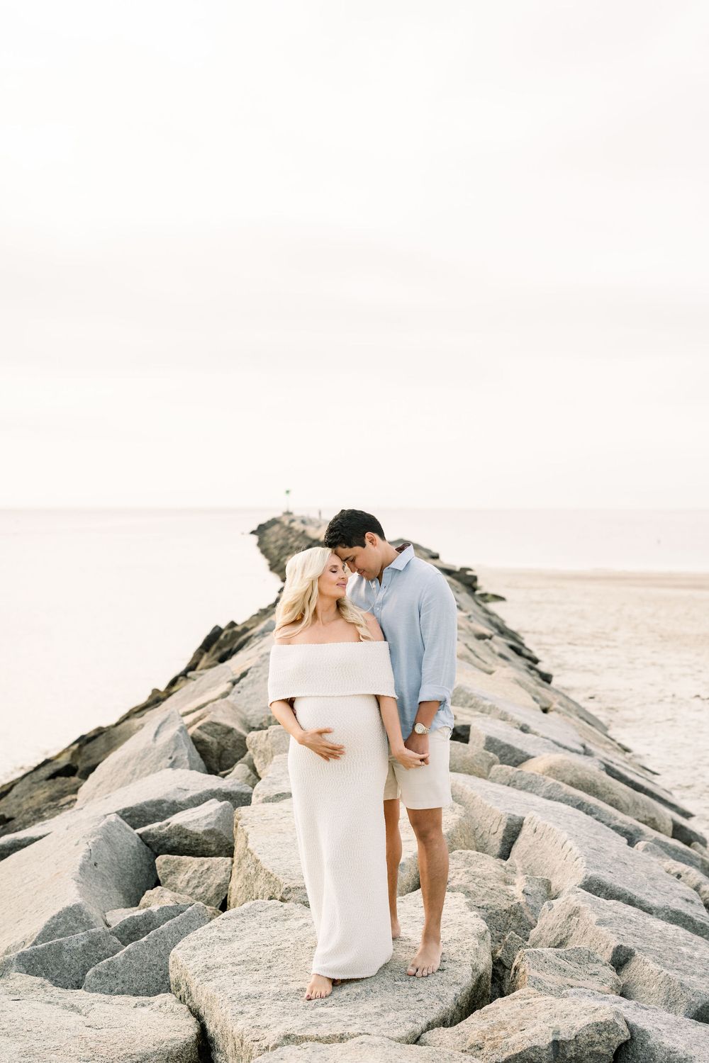 A couple walks along a rocky jetty at the beach during sunset creating a romantic coastal scene.