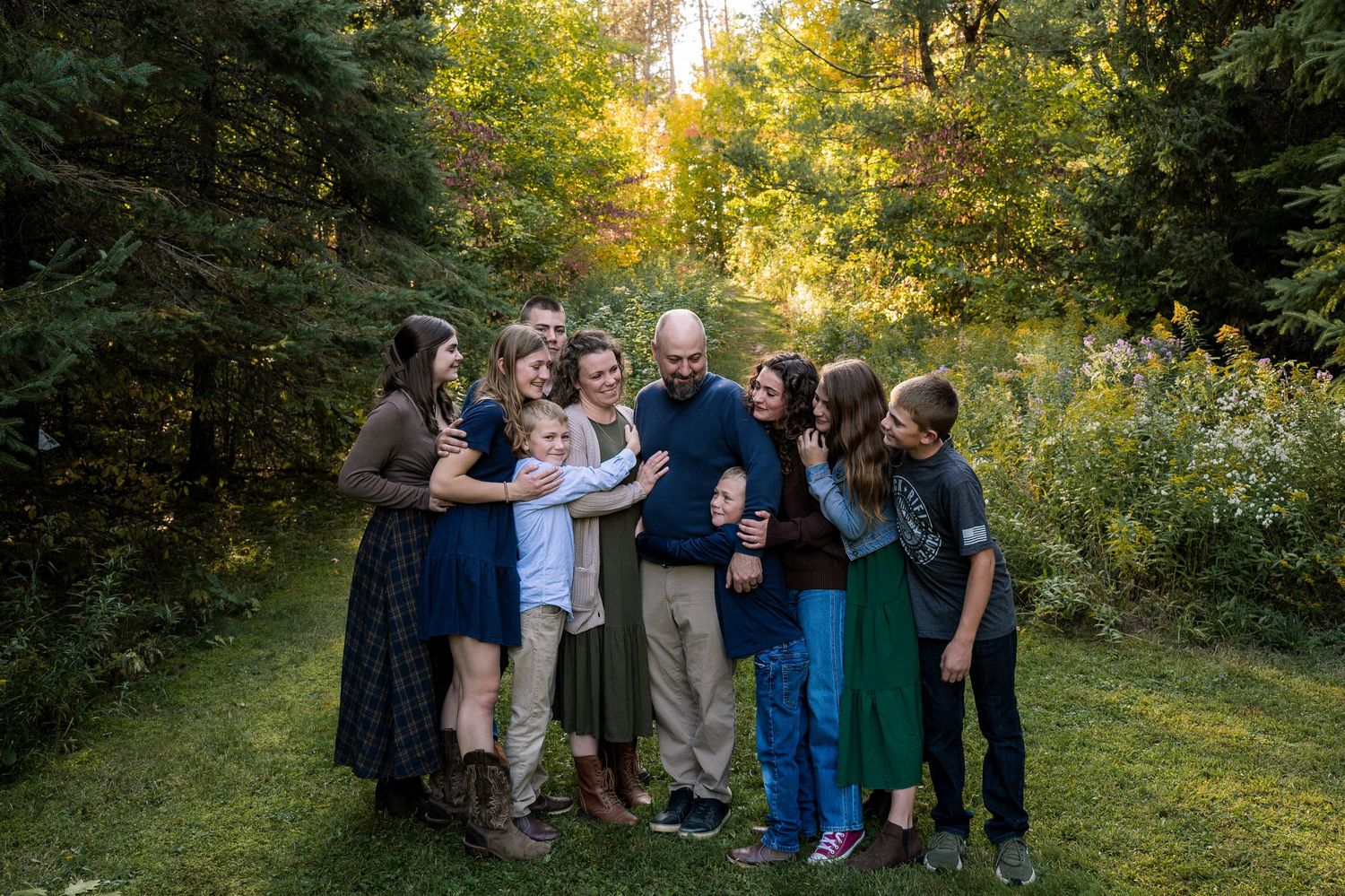 A group of people gathered outdoors in a wooded area during golden hour sunlight.