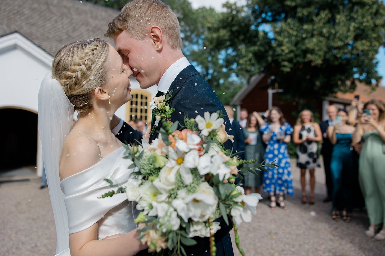 A wedding couple shares a romantic moment outdoors surrounded by guests throwing confetti during their celebration.