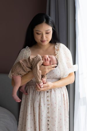 Professionele newborn fotograaf legt pasgeboren baby vast tijdens newbornshoot met zachte styling en natuurlijke poses in Eindhoven.