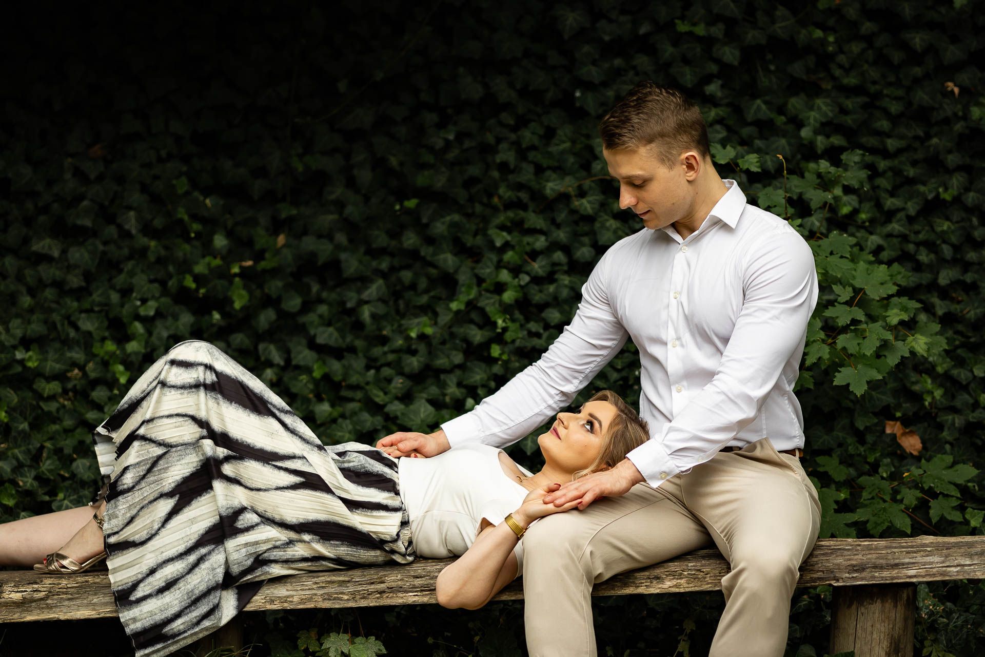 Couple sharing an intimate moment while sitting on a wooden bench surrounded by greenery.
