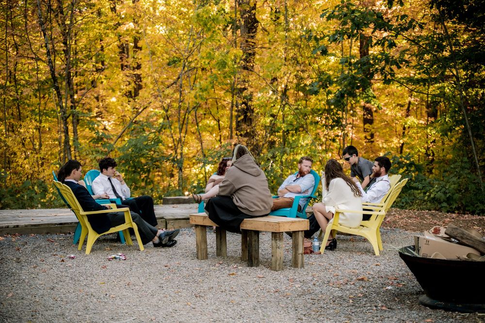 Yellow Adirondack chairs arranged in a circle on gravel ground surrounded by autumn trees with golden foliage.