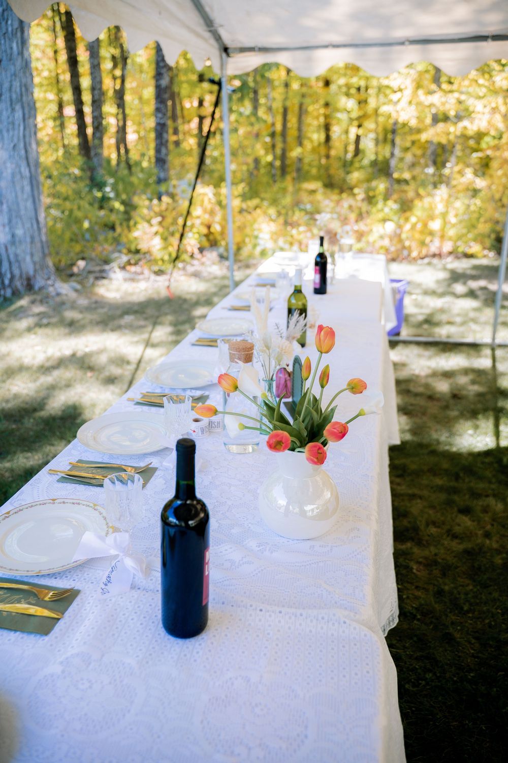An elegant outdoor table setting with white linens, wine bottles and colorful tulip centerpieces in natural sunlight.