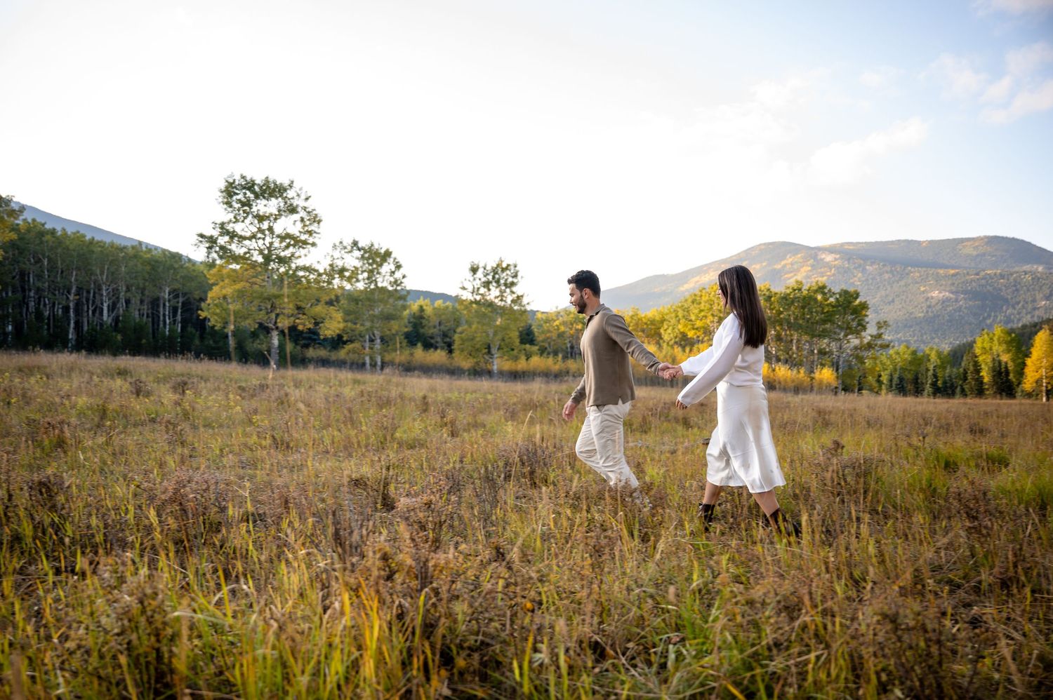 A couple embraces romantically in a golden mountain meadow during autumn with mountains in the background.