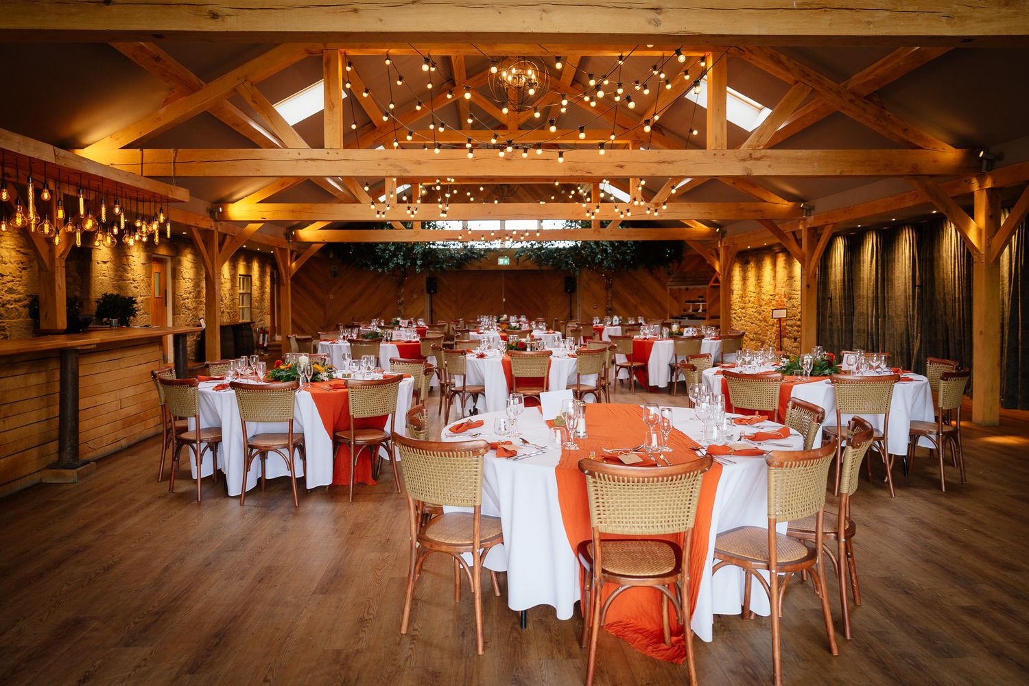 Elegant reception hall with wooden beams and chandeliers set with round tables in warm lighting.