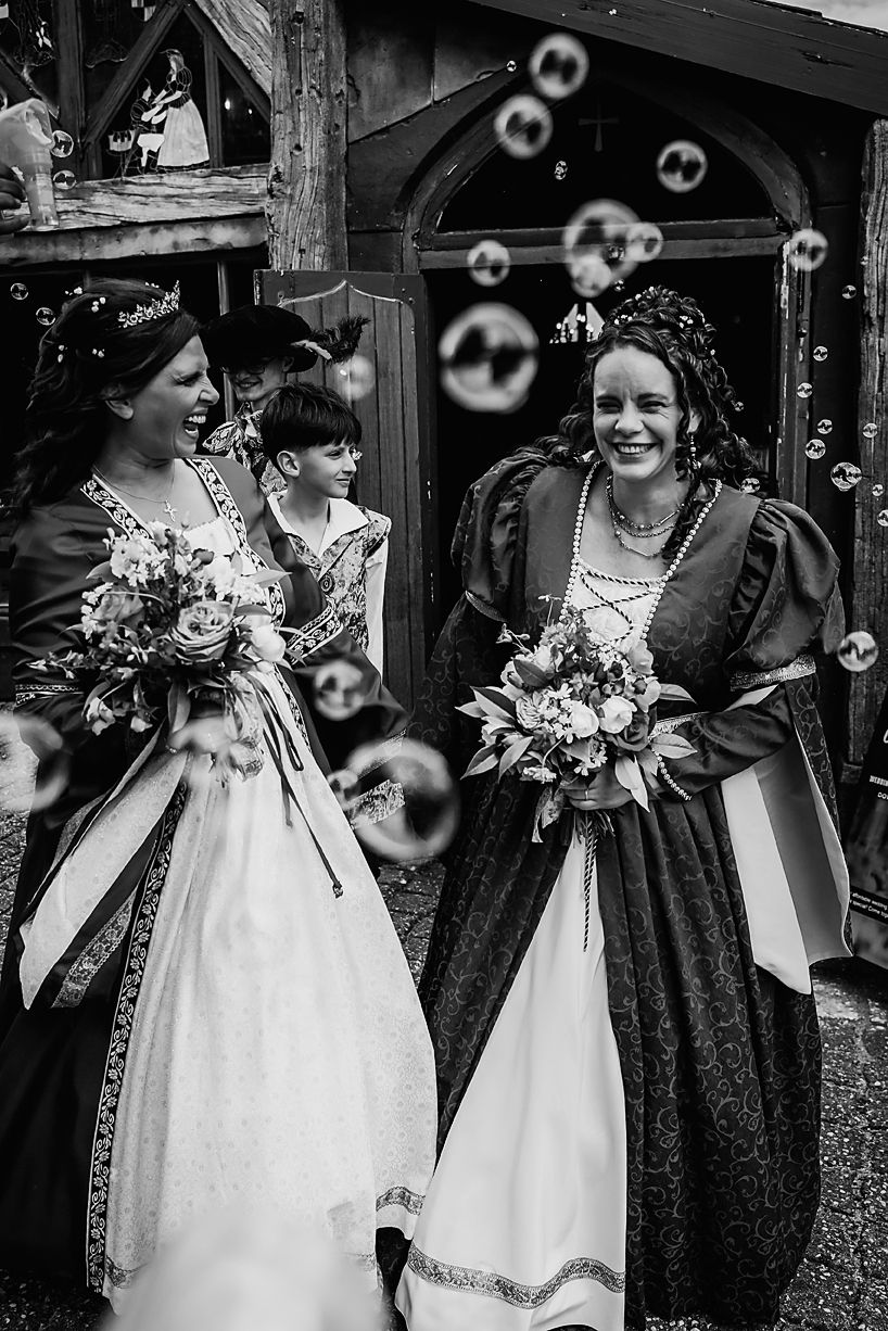 A group in vintage-style dresses stand together while soap bubbles float through the black and white scene.