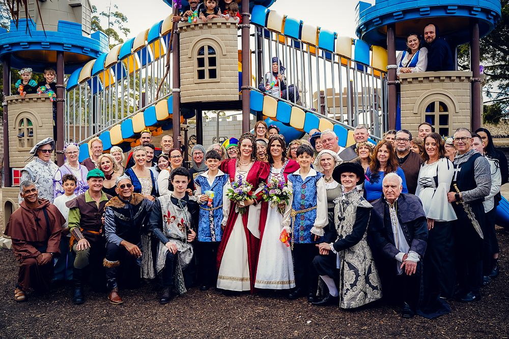 Large group of wedding guests gather outside historic building with blue and yellow banners for celebratory photo.