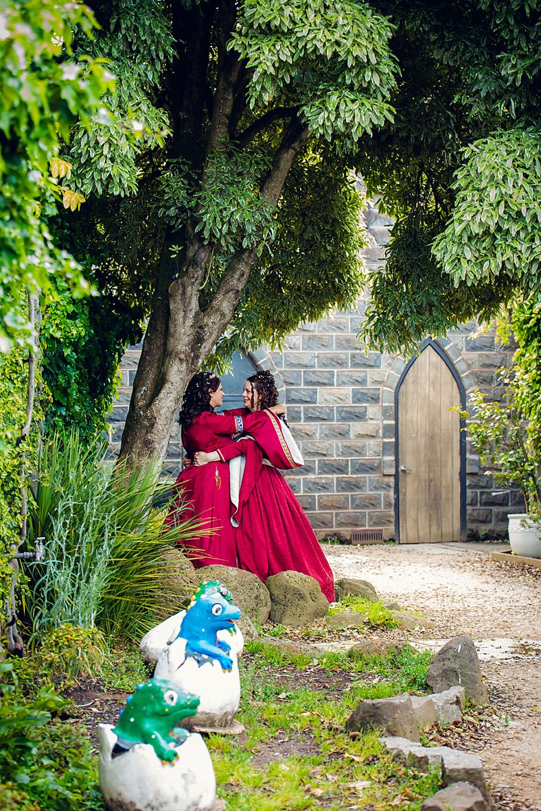 Garden pathway with decorative blue, green, and white gnome sculptures nestled among lush foliage and stone walls.