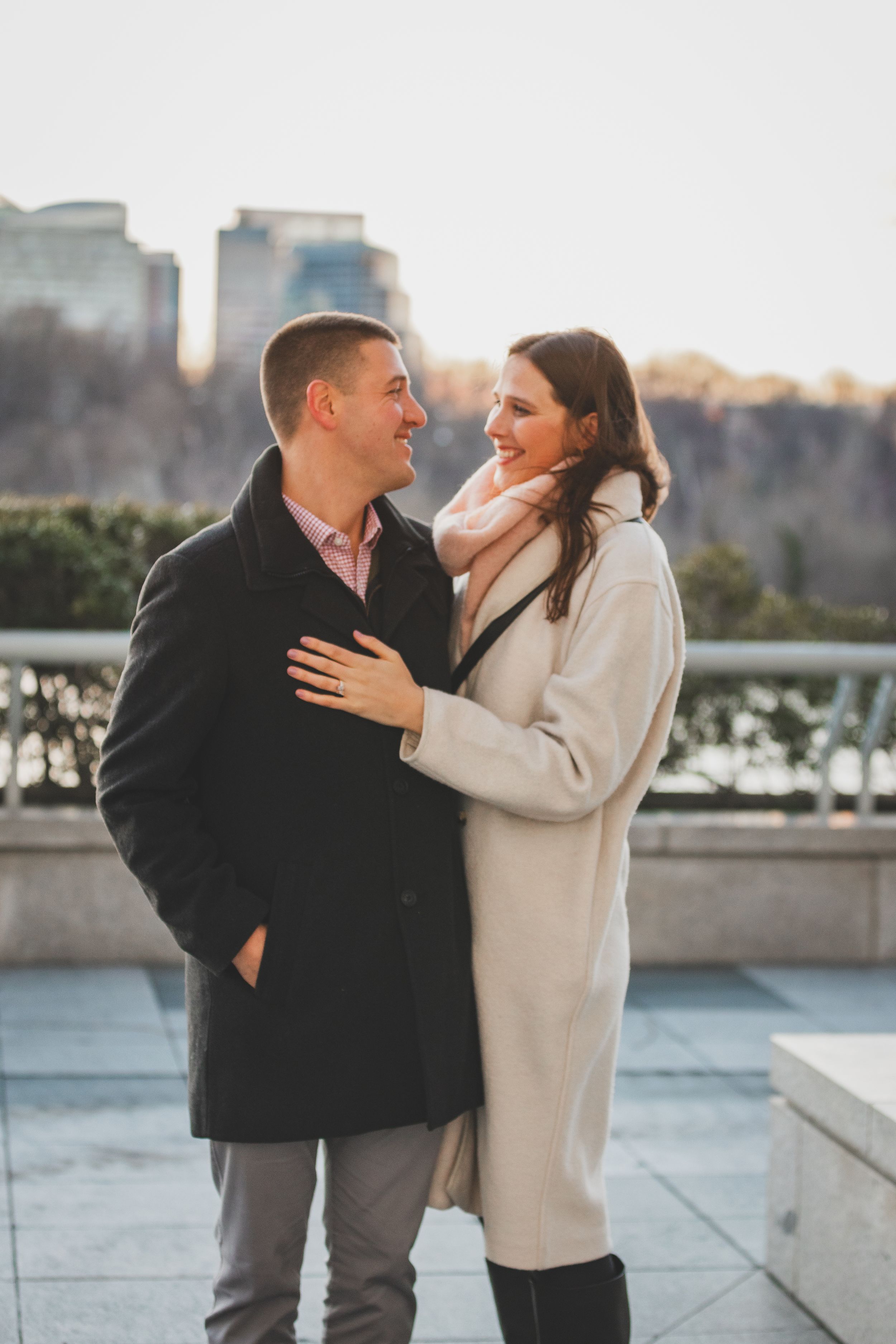 A couple shares a romantic moment during a winter engagement photoshoot along a city waterfront at the Kennedy Center