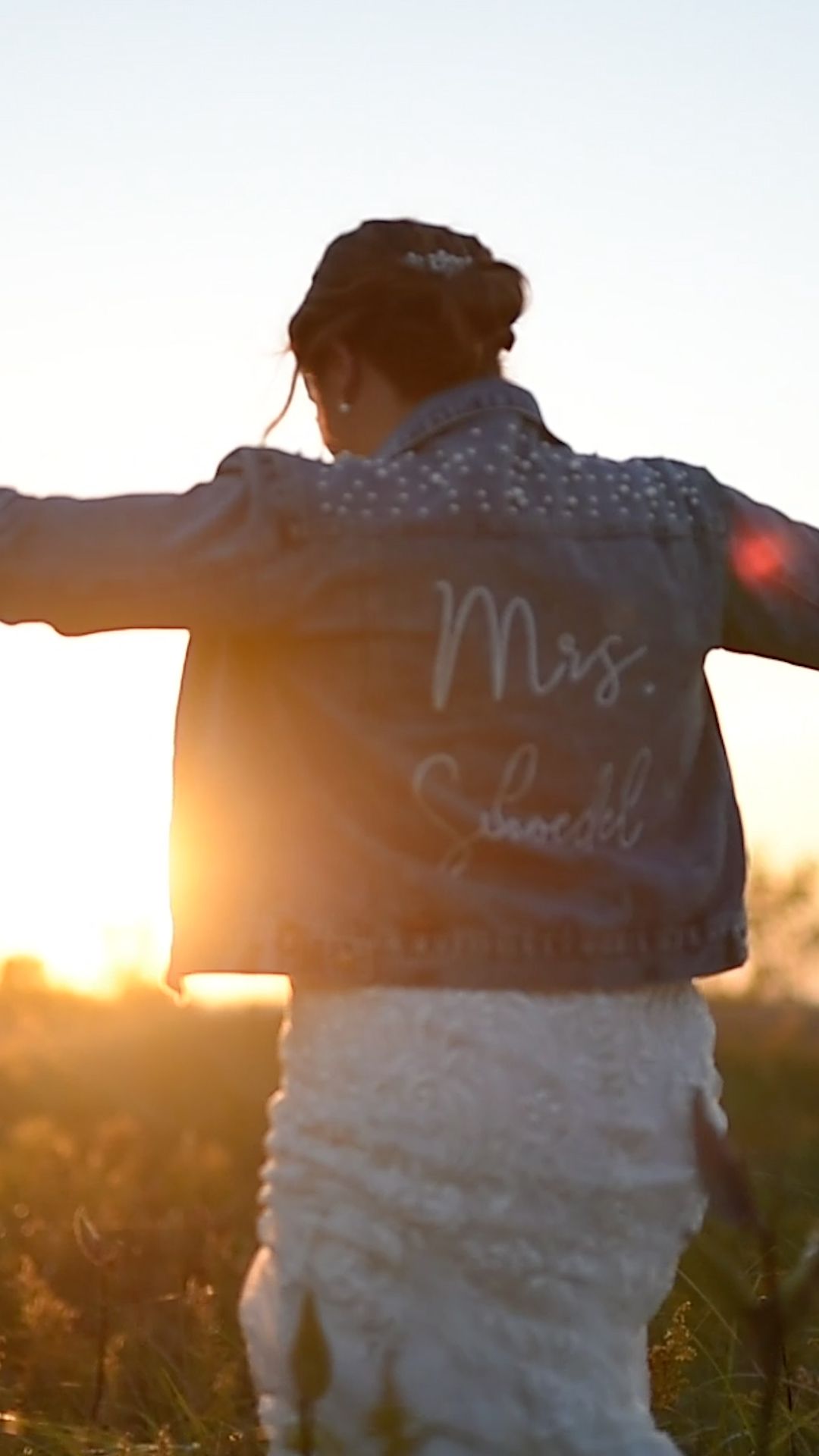 A silhouetted figure in a white dress stands with arms outstretched against a golden sunset in a field.