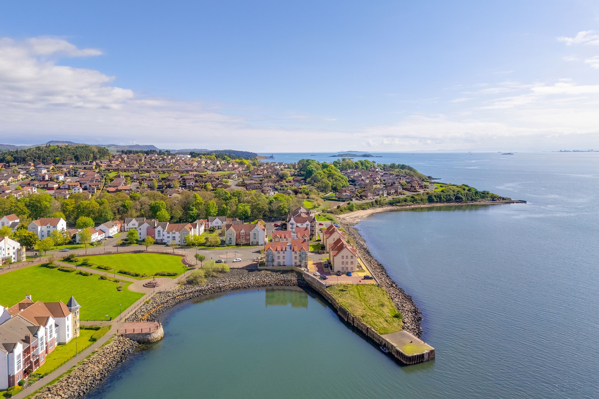Panoramic aerial view of a coastal town with colorful buildings and a curved harbor along the Scottish shoreline.