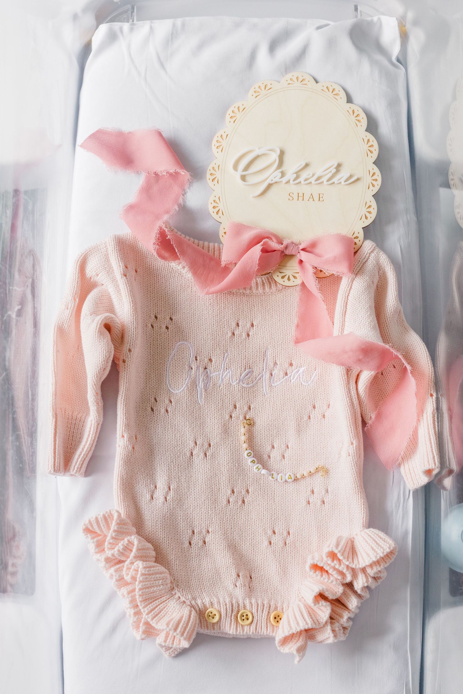 Delicate pink baby sweater with floral lace trim and matching booties displayed in clear packaging at a newborn session in Pittsburgh, PA.