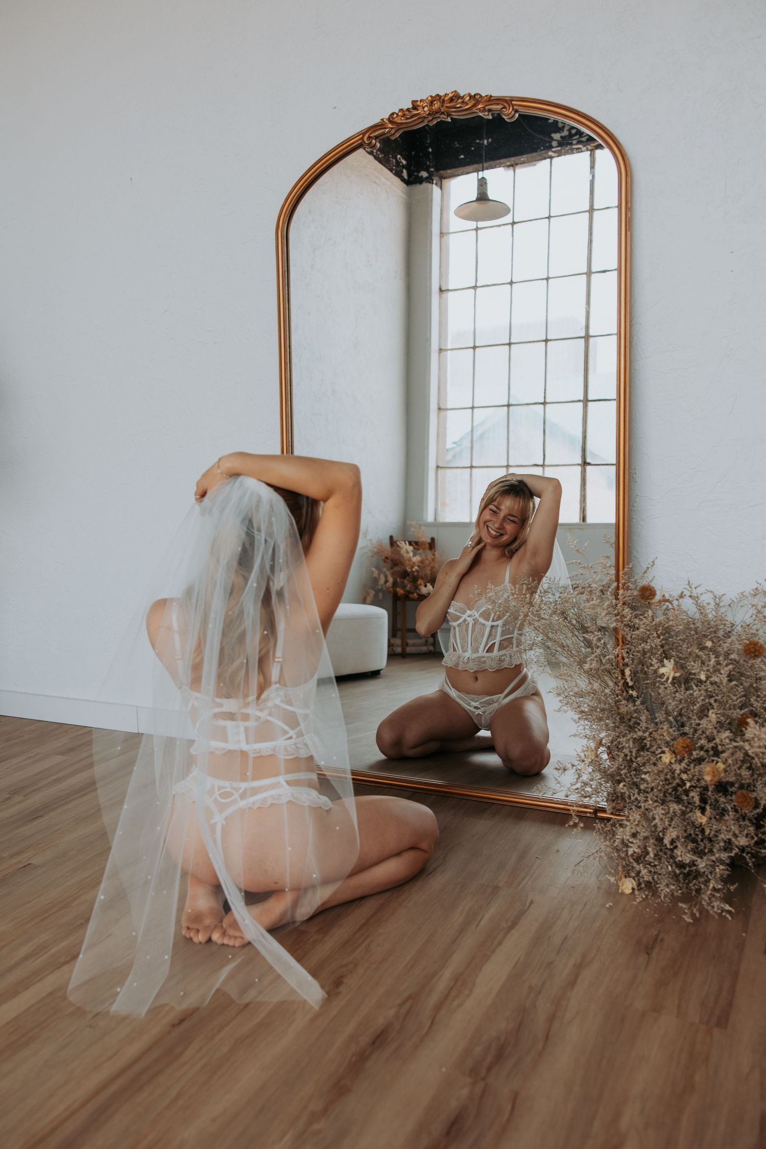 Artistic boudoir photoshoot series featuring delicate poses with a mirror and dried floral arrangements on wooden floors.