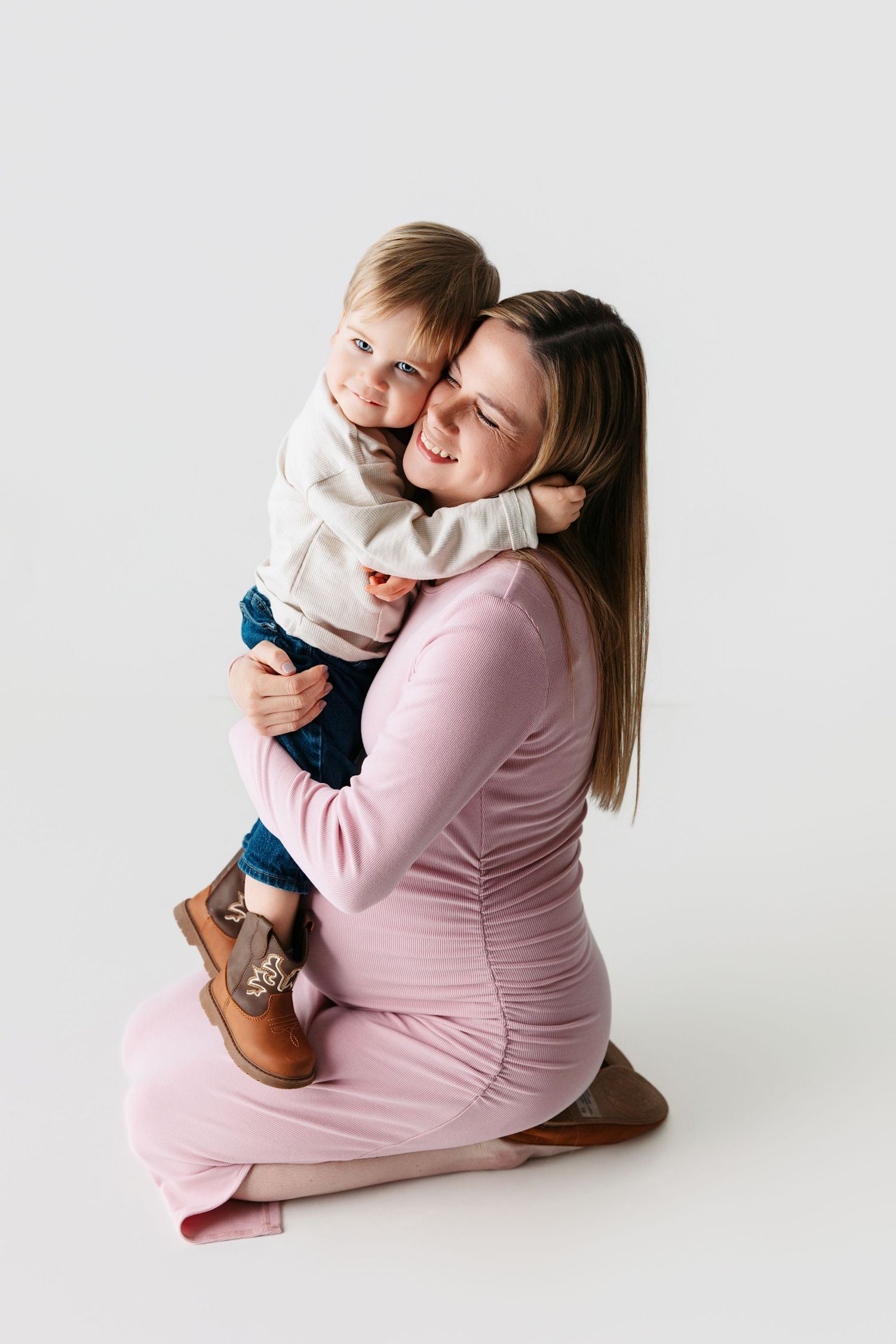 Expectant mom and toddler in matching pink and cream outfits against a white studio backdrop. Middle Tennessee maternity photography session