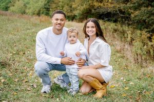 A family dressed in white sits together on grassy hill during golden autumn afternoon.