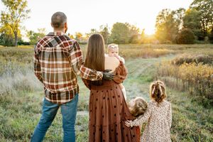 Family walking together through tall grass in a golden meadow at sunset.