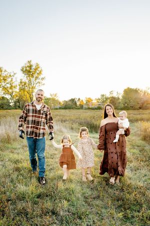 family walking through a rustic field wearing coordinated autumn colors during sunset.