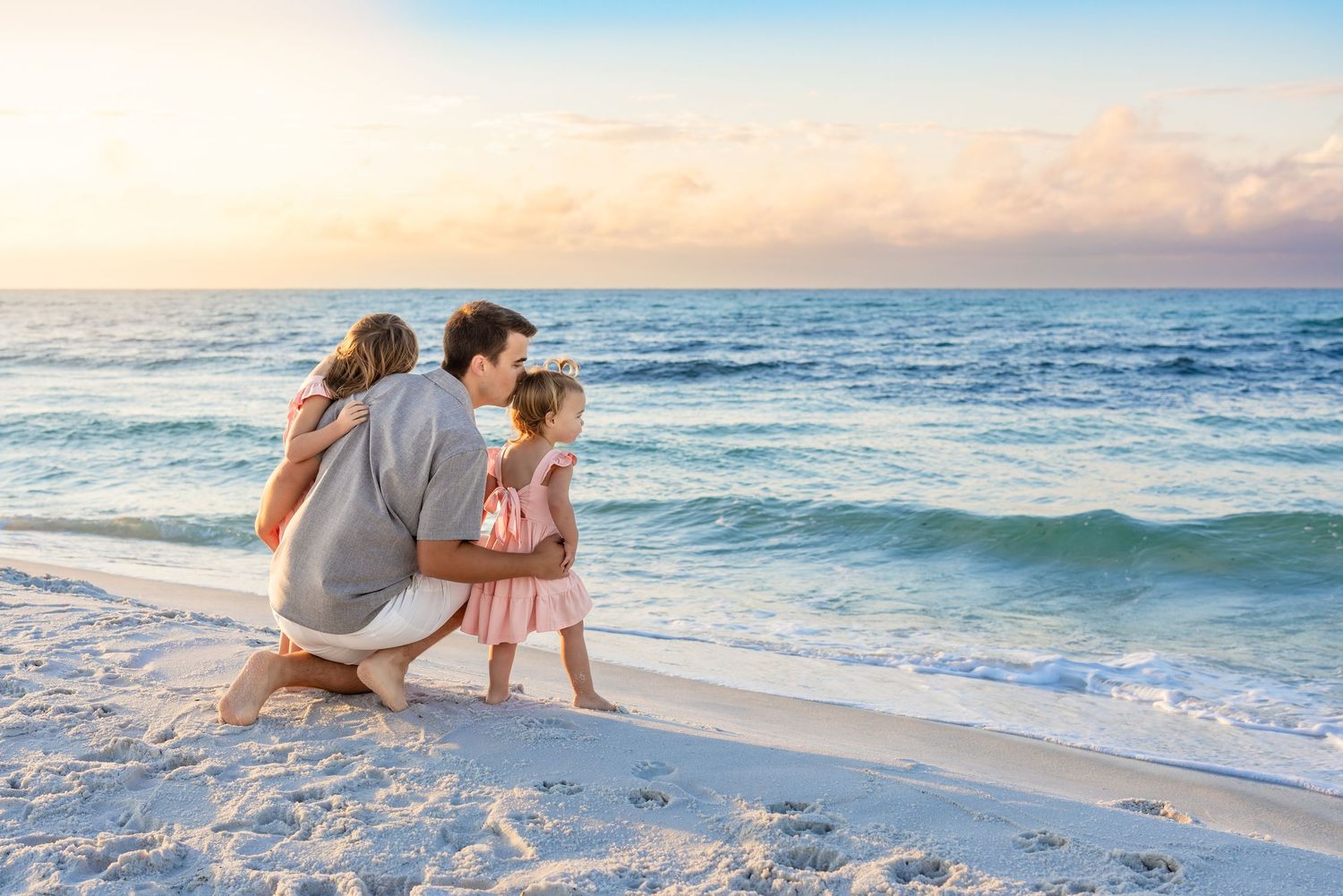 Family walking together along a beautiful white sandy beach at sunset with ocean waves in the background.