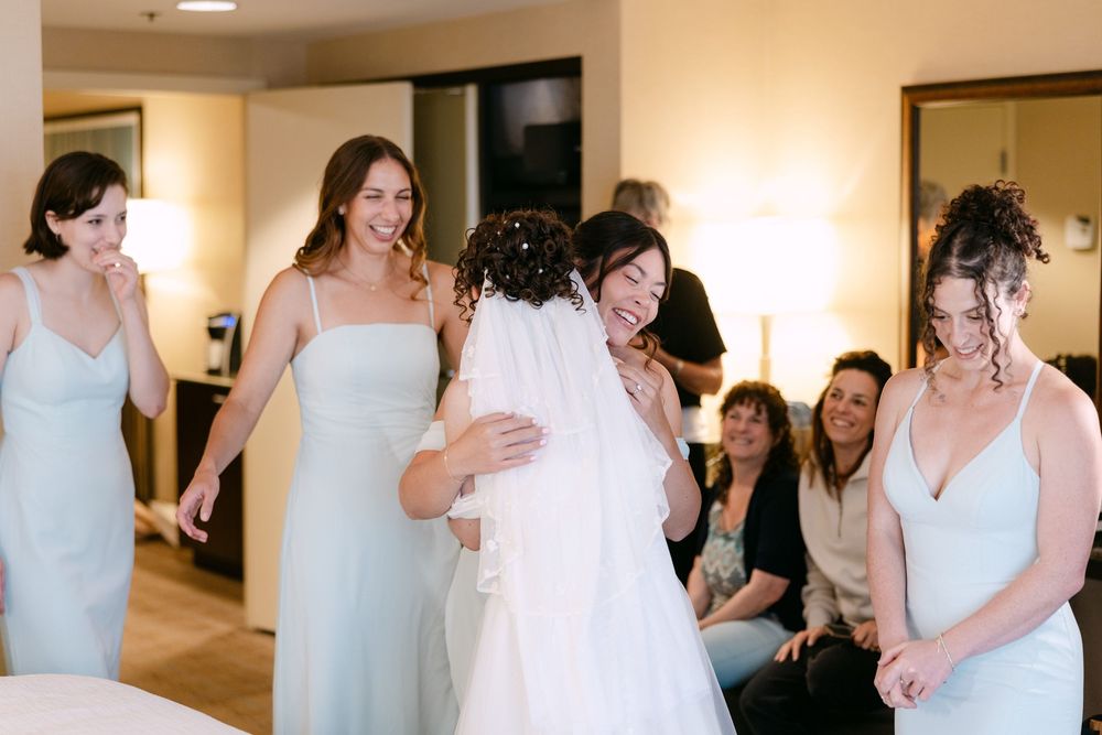 Bridesmaids in light blue dresses gather together during wedding preparations in a warmly lit room.