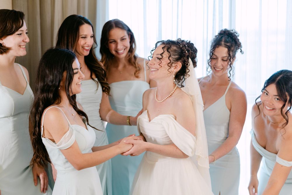 A group of bridesmaids in light blue and white dresses pose together at a wedding celebration.