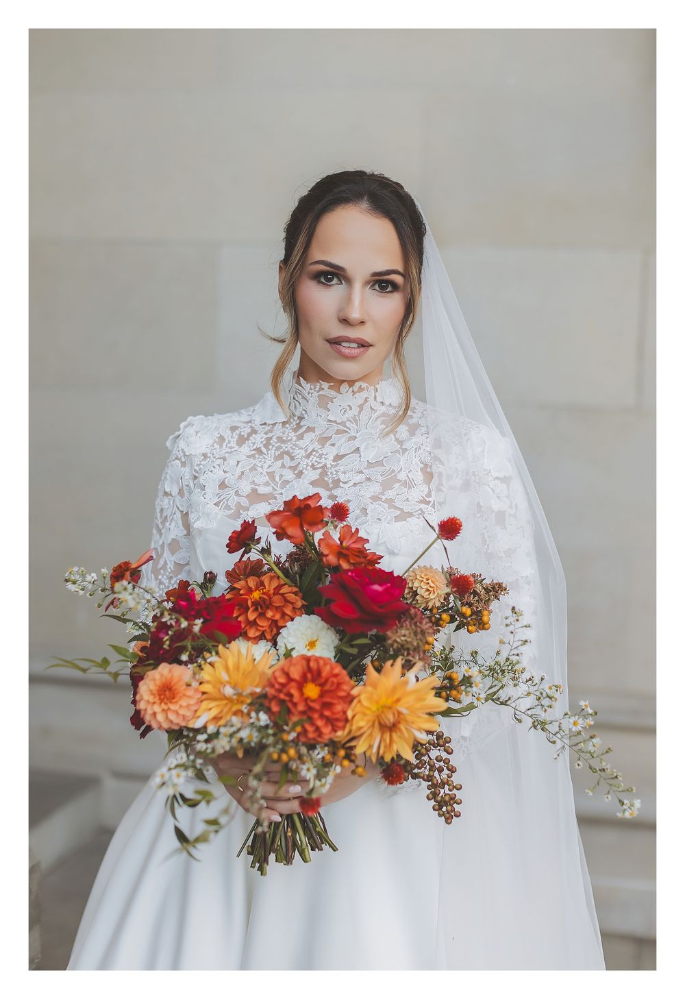 A beautiful bridal bouquet featuring orange, red and yellow dahlias with delicate white flowers against a light backdrop.