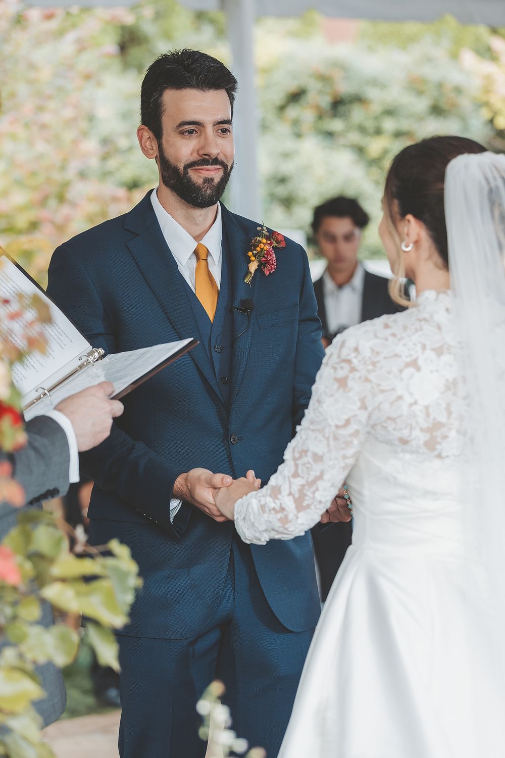 A couple exchanges vows during an outdoor wedding ceremony with the groom wearing a navy suit and gold tie.