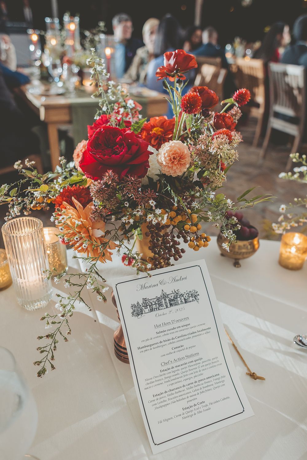 Wedding reception table settings with elegant floral centerpieces, menu cards, and glowing candles in glass holders.