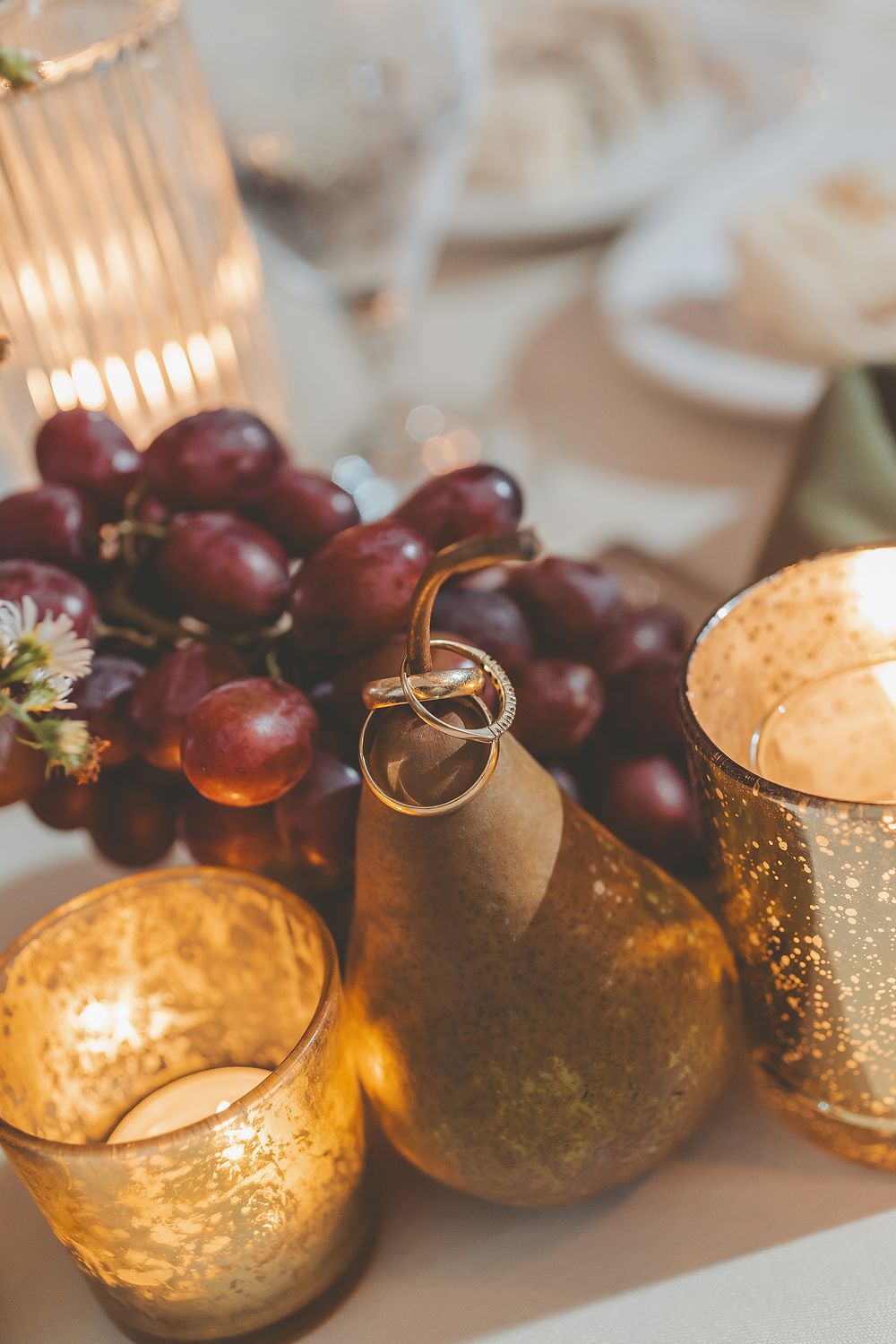 Wedding rings rest elegantly beside golden candleholders and purple grapes on a romantic table setting.