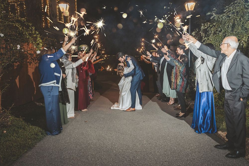 Wedding guests celebrate with sparklers at night during an outdoor reception celebration.