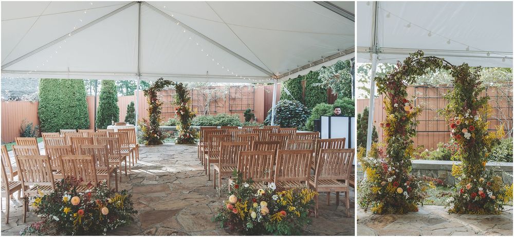 A white wedding tent with wooden chairs and floral arches set up for an outdoor ceremony on a grassy lawn.