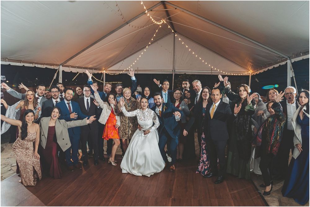 Wedding guests celebrate together under a white tent with string lights during an evening reception celebration.