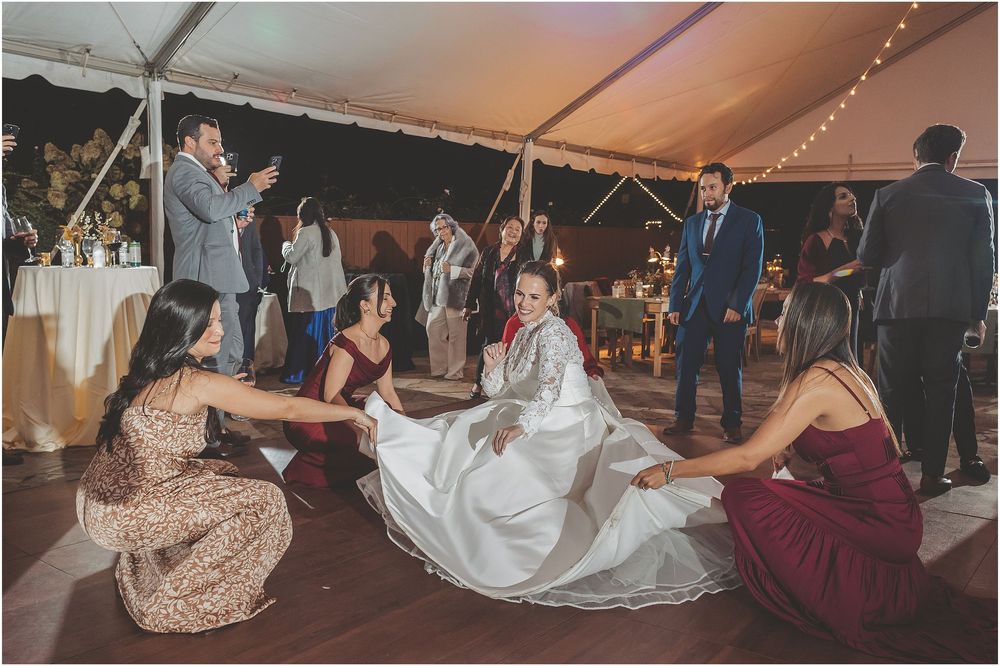 Wedding guests dance together on the floor during a reception celebration under a white tent with string lights.