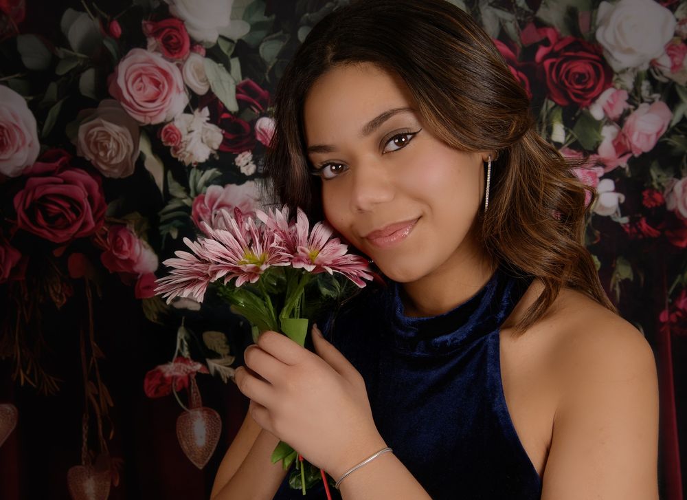 Romantic portrait against floral backdrop with pink and red roses in a dark moody setting.