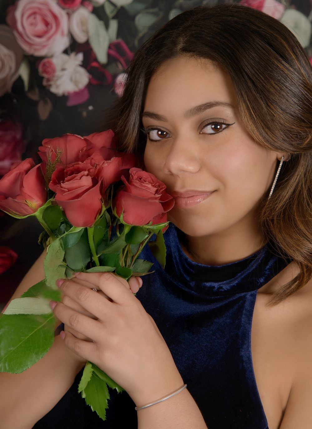 A person in a navy top poses with red roses against a dark background in a romantic portrait series.