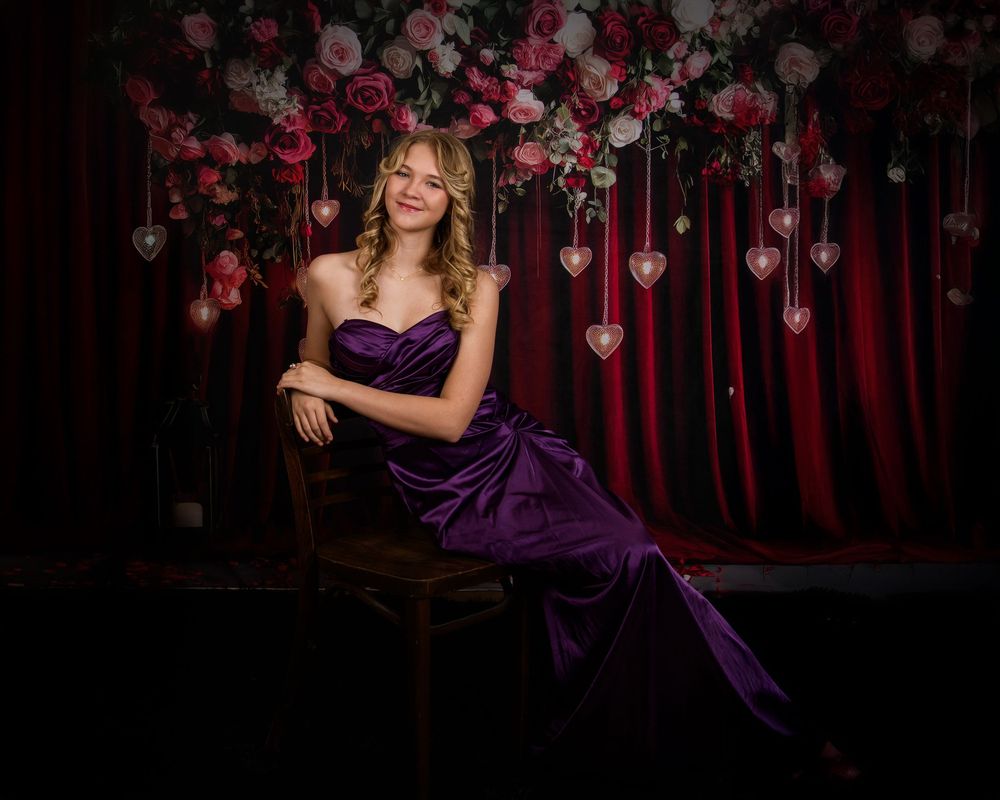 A figure in an elegant purple gown poses against a romantic backdrop with hanging heart decorations.