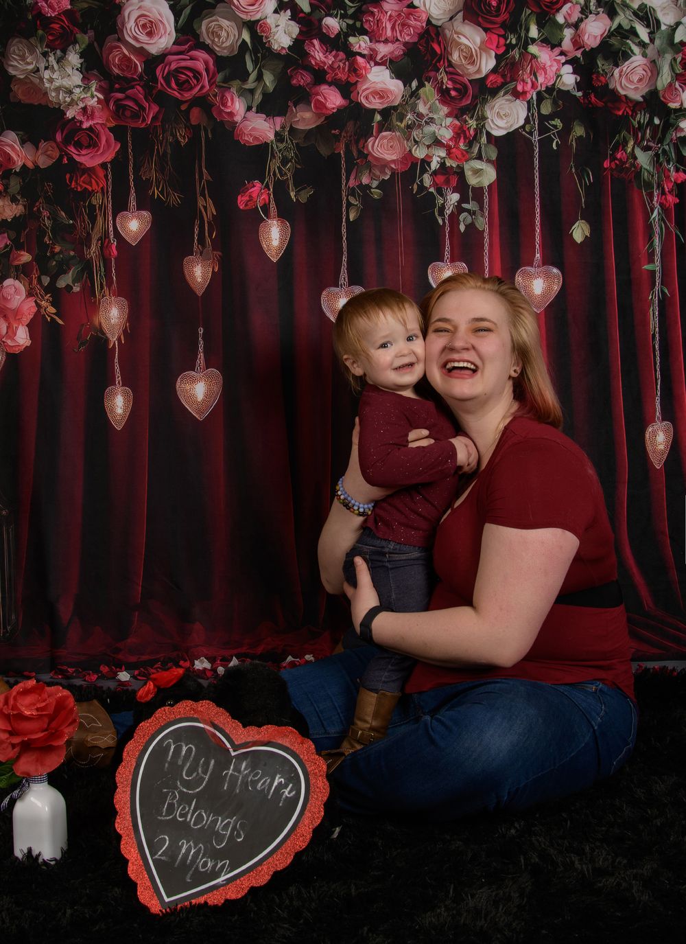 Romantic Valentine's photo session with pink roses and hanging heart decorations against a dark backdrop.