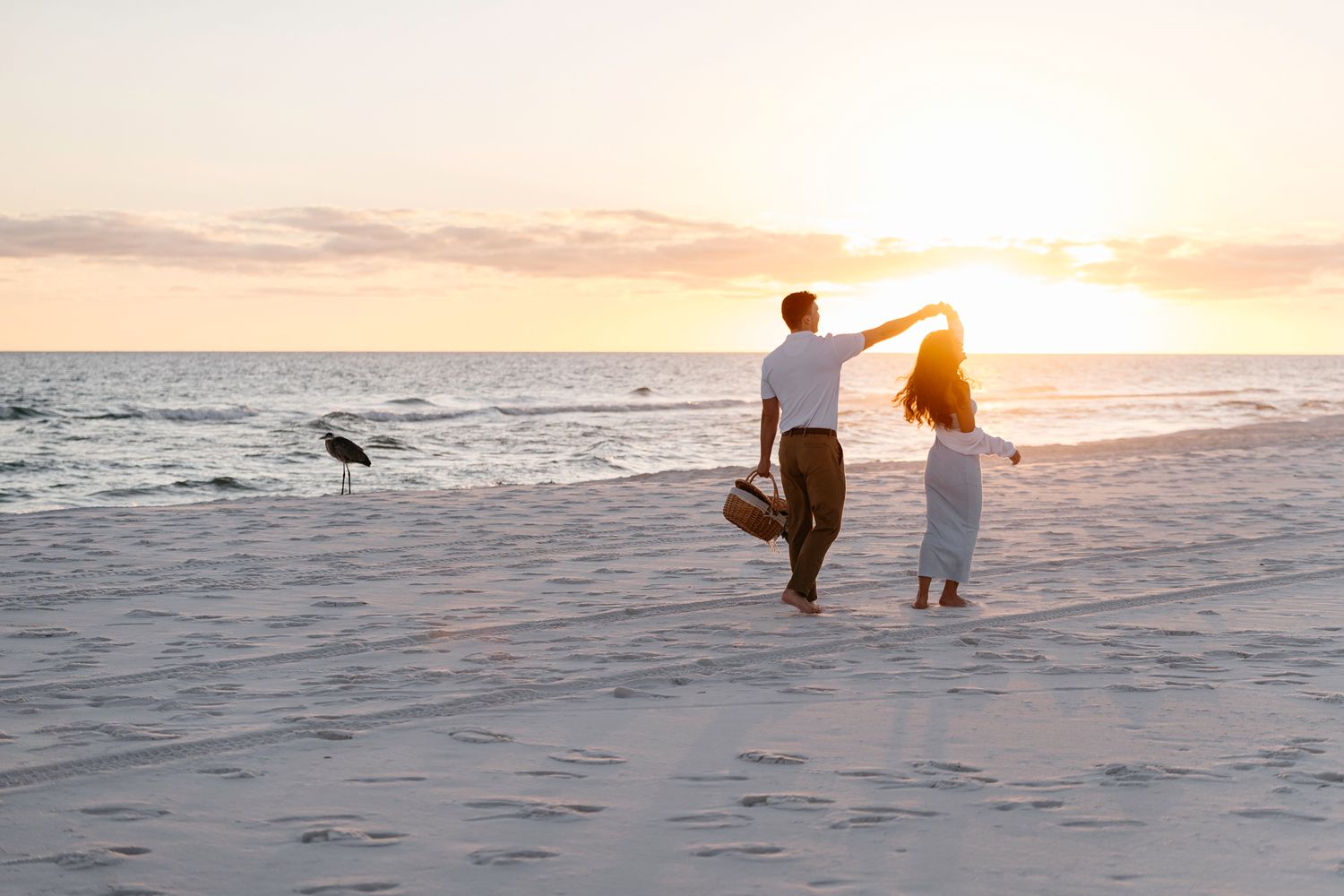 A couple walks along a serene beach at sunset with waves crashing in the background.