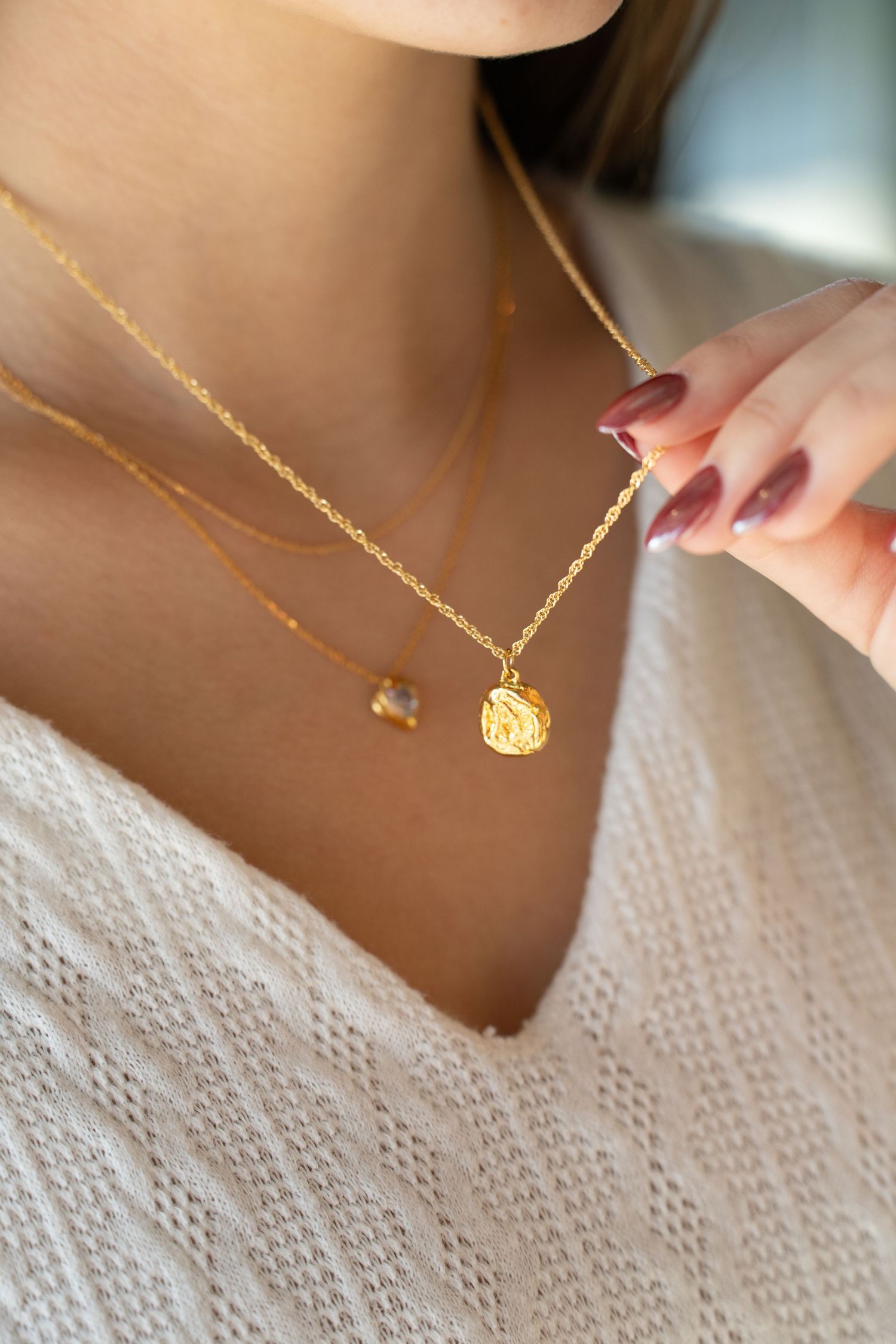Close-up of delicate gold pendant necklaces with heart and coin charms layered on white lace fabric.