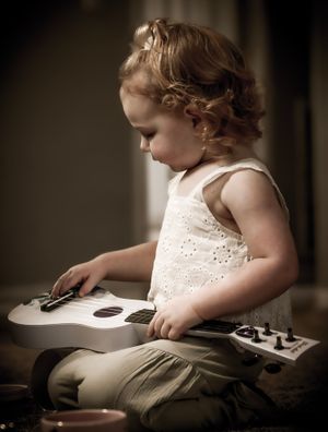A young child in a white eyelet dress examines a book while sitting in soft, moody lighting.