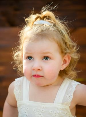 A young child in a white eyelet dress looks up with bright blue eyes and wispy blonde hair.